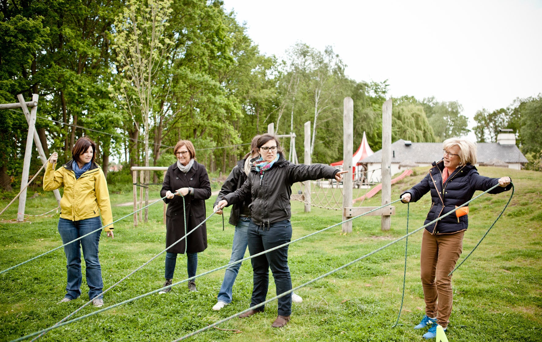 Cinq femmes debout sur l'herbe en plein air, tenant et tirant des cordes ensemble dans le cadre d'une activité d'équipe.