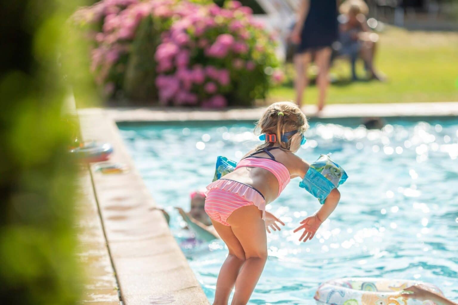 Little girl in pink bikini, ready to jump in the swimming pool